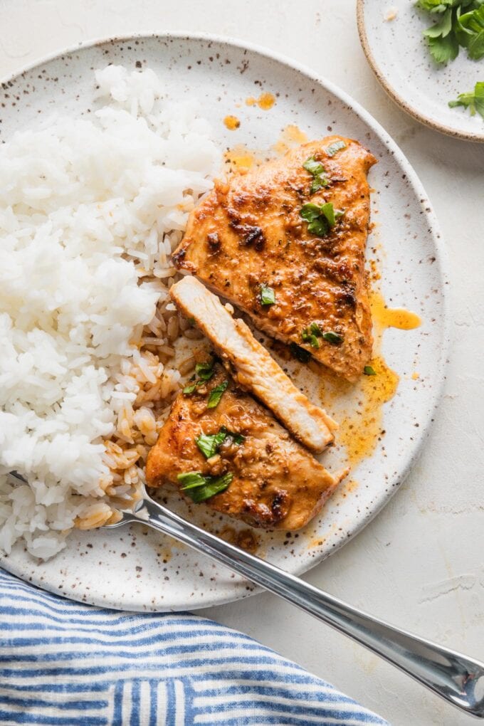 A thin-sliced chicken breast cooked with Cajun butter sauce and plated alongside white rice, with one slice cut to reveal a moist, tender interior.