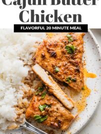 Cajun butter chicken breast with plenty of sauce, parsley for garnish, and a side of white rice on a white ceramic plate.