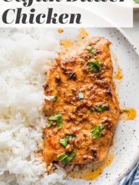 Cajun butter chicken breast with plenty of sauce, parsley for garnish, and a side of white rice on a white ceramic plate.