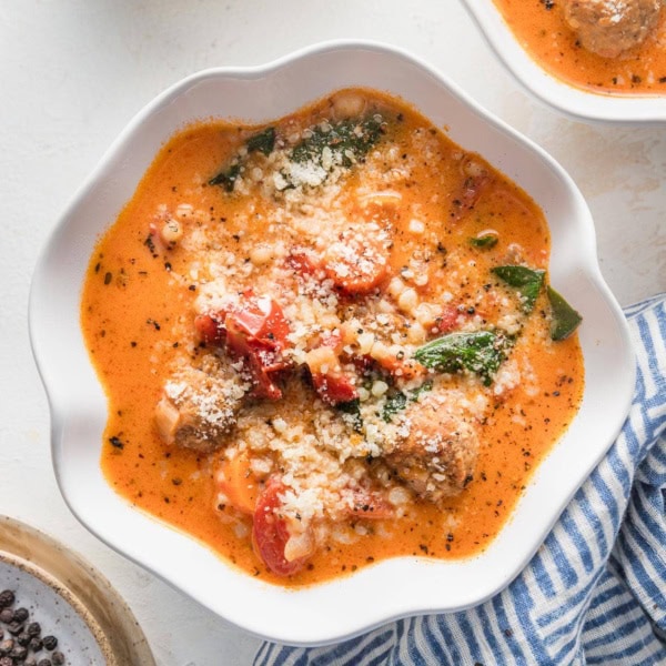 Small white bowls filled with creamy tomato meatball soup with extra Parmesan and black pepper in the background for garnish.