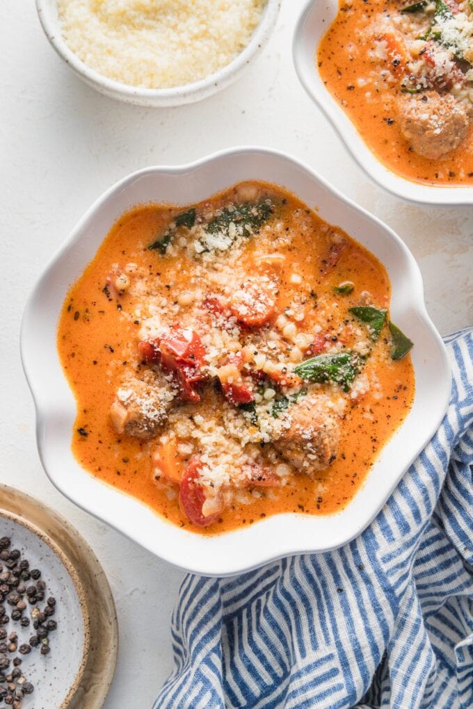Small white bowls filled with creamy tomato meatball soup with extra Parmesan and black pepper in the background for garnish.
