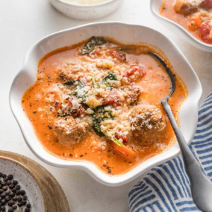 Angled view of creamy tomato meatball soup served in small bowls.