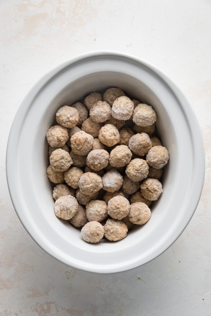 White ceramic slow cooker bowl filled with frozen miniature meatballs.