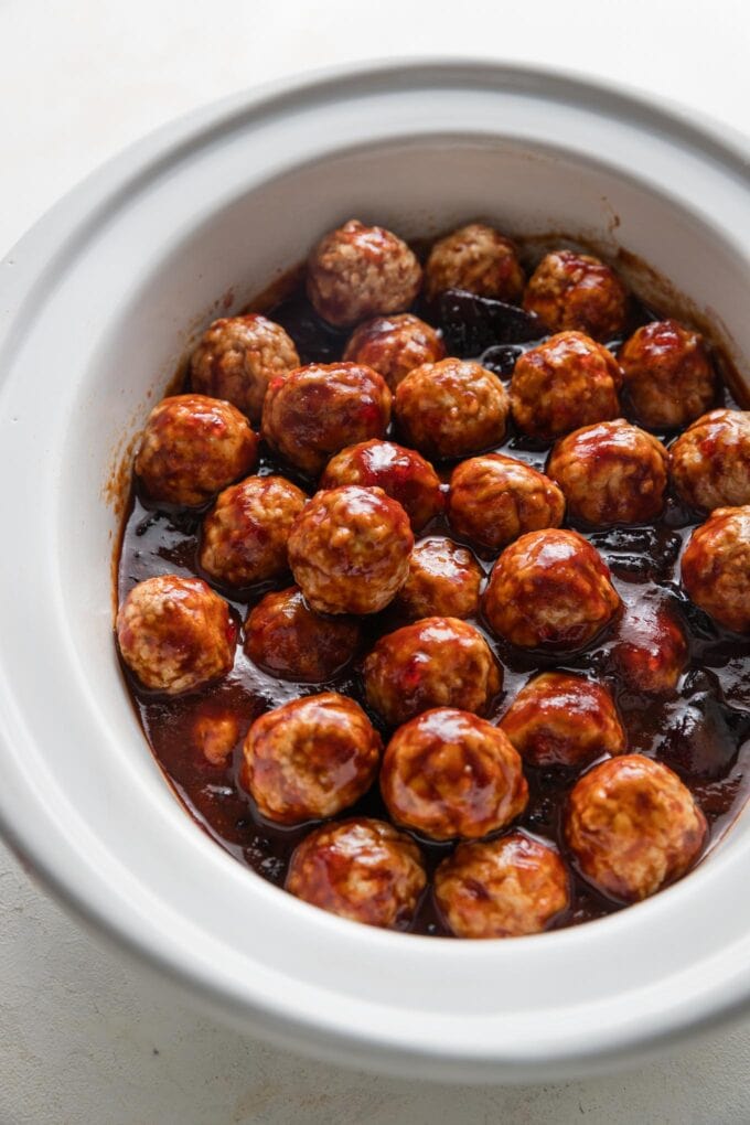 Mini meatballs cooked in a small white slow cooker with a sweet and savory BBQ-grape jelly glaze.