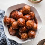 Bowl full of grape jelly BBQ meatballs cooked in the slow cooker and served as an appetizer with toothpicks and green onions nearby on the counter.