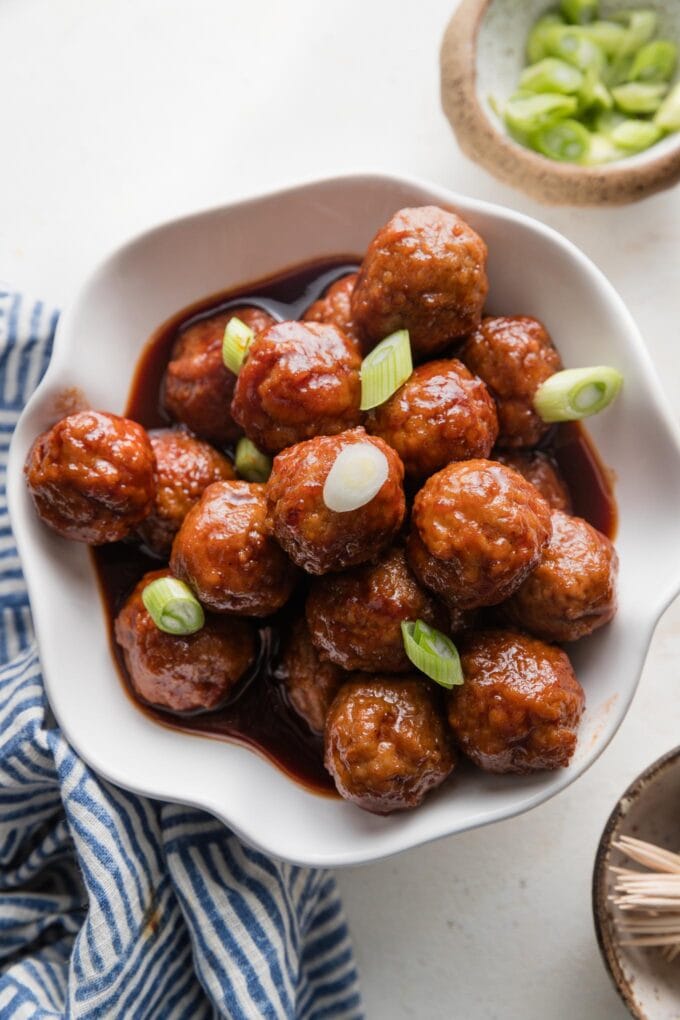 Bowl of slow cooker BBQ meatballs served with thinly-sliced green onions on top as a garnish.