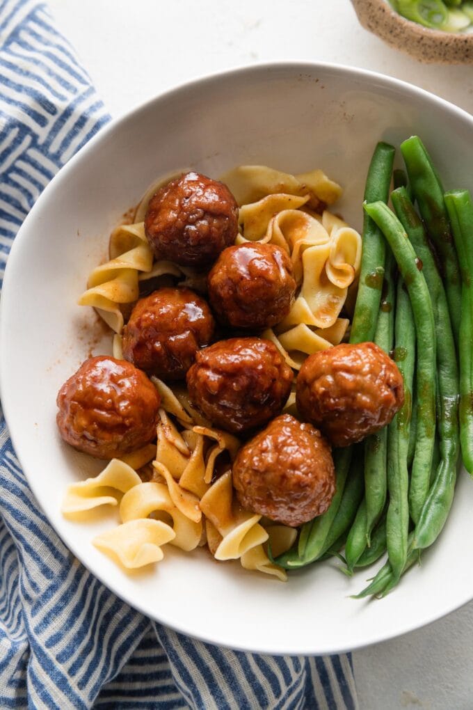 Bowl full of egg noodles, green beans, and Crockpot BBQ meatballs served with a BBQ-grape jelly sauce.
