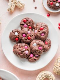 Small white plate on a pink counter, filled with double chocolate cookies with Valentines M&Ms and chocolate chips.