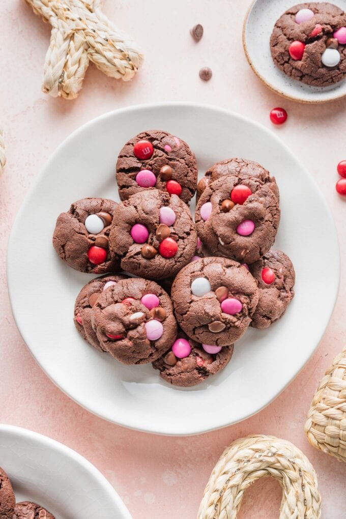 Small white plate on a pink counter, filled with double chocolate cookies with Valentines M&Ms and chocolate chips.