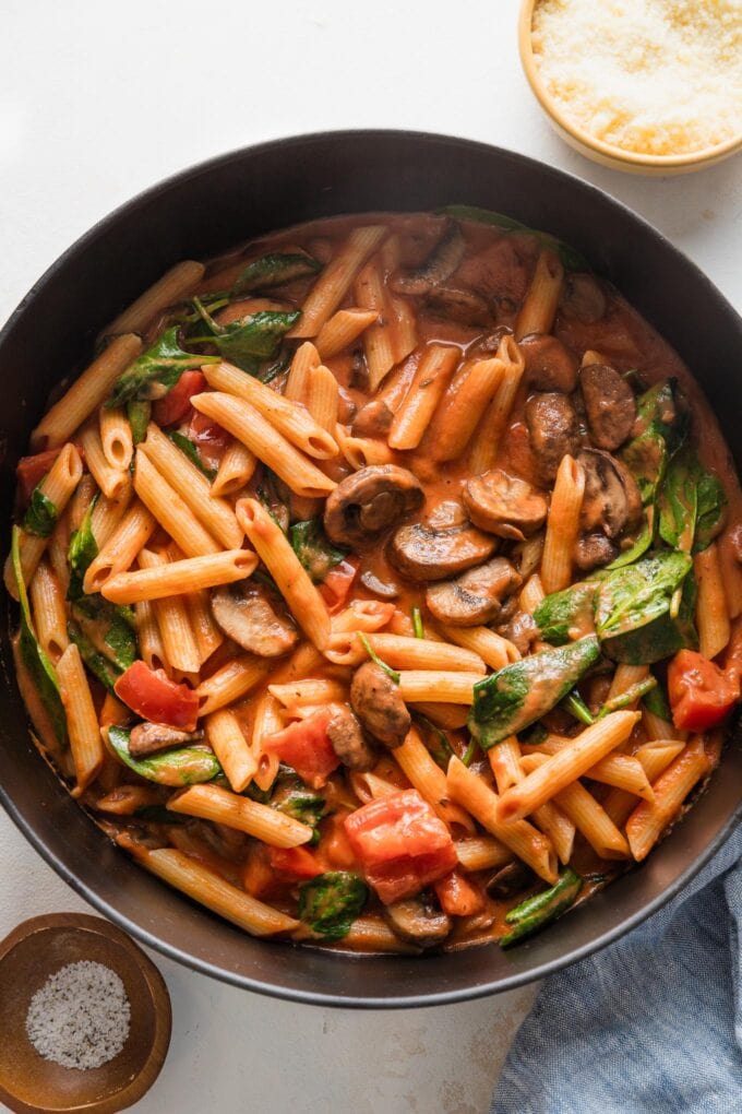 Penne pasta added to skillet with vegetables and creamy tomato sauce.