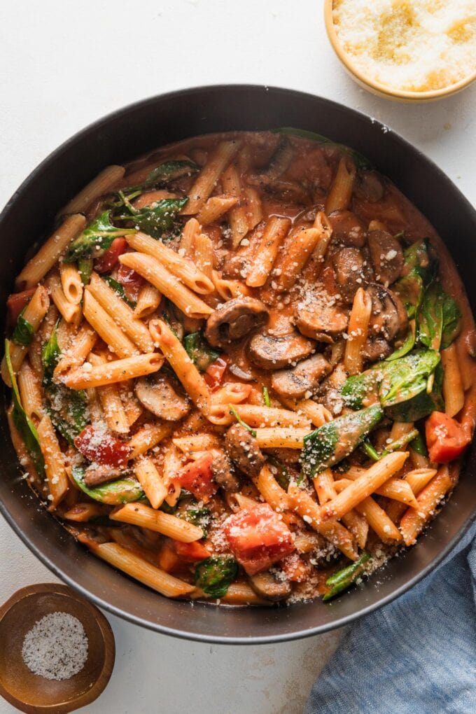 Cast iron skillet filled with a homemade penne rosa garnished with Parmesan.