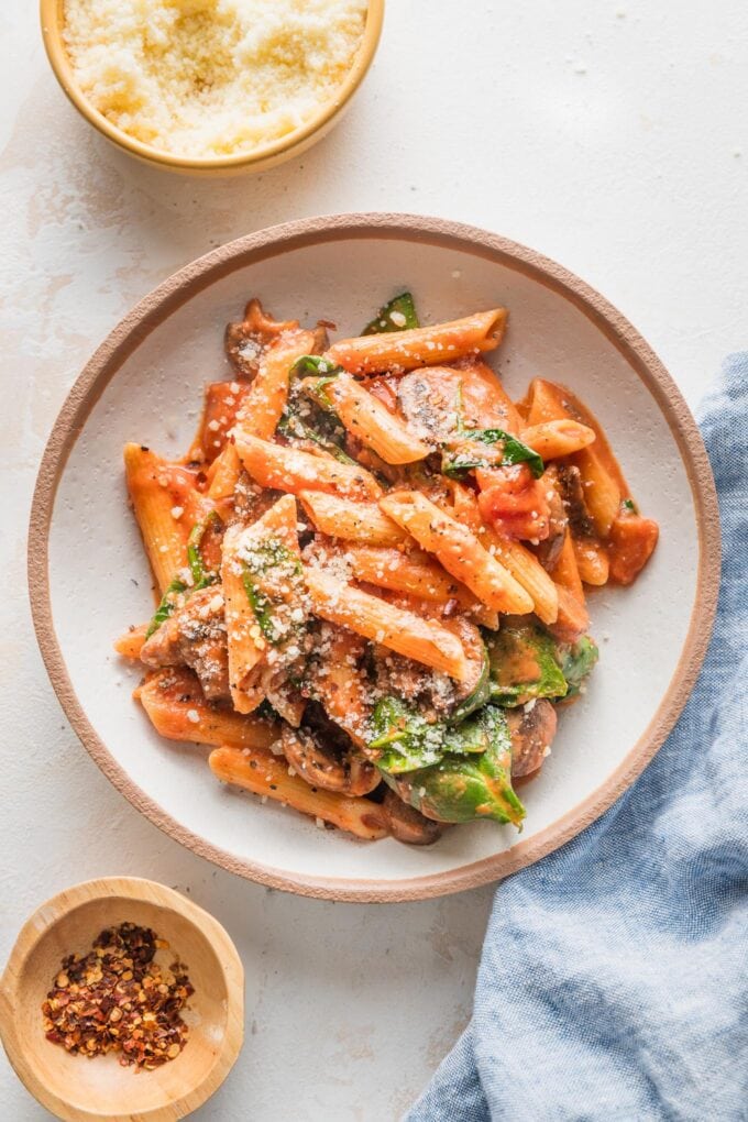 Small serving bowl filled with a helping of penne Rosa, a Noodles & Co. copycat recipe, garnished with extra Parmesan and red pepper flakes.