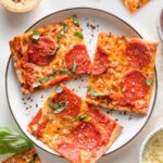 Small black-rimmed white plate with three pieces of pepperoni flatbread pizza.