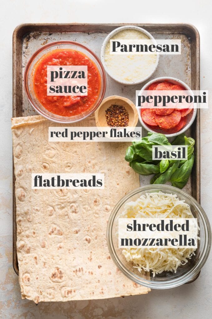 Labeled overhead photo of lavash-style flatbreads, pizza sauce, mozzarella and Parmesan cheese, pepperoni, red pepper flakes, and fresh basil.