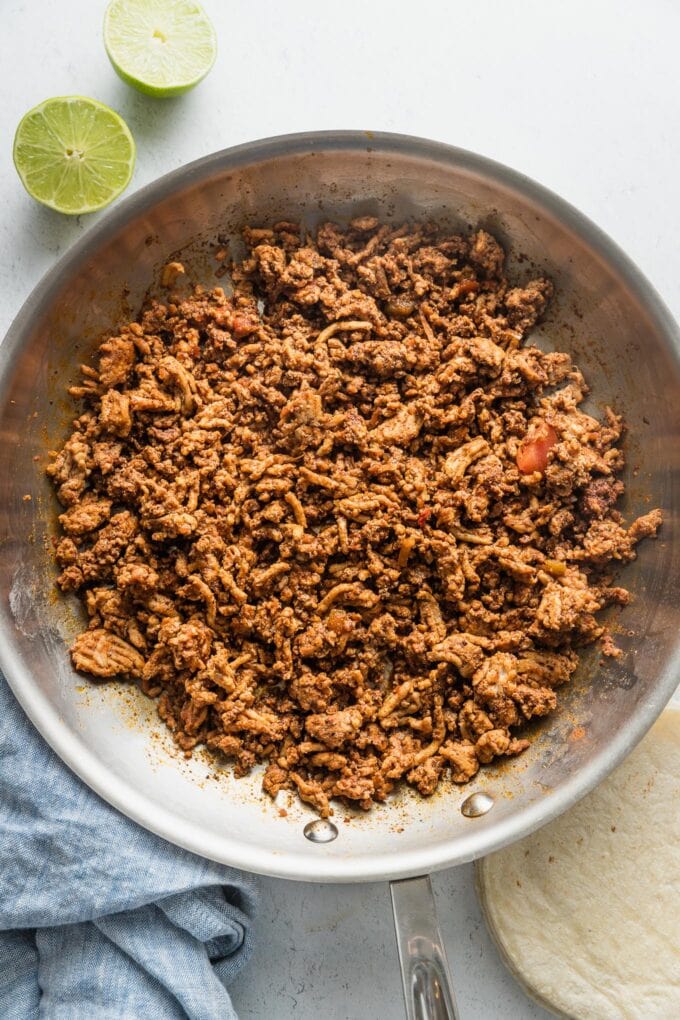 Overhead view of a large aluminum skillet filled with cooked ground chicken taco meat.