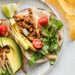 Close up of a ground chicken taco plated with avocado, tomato, cheese, and lettuce.