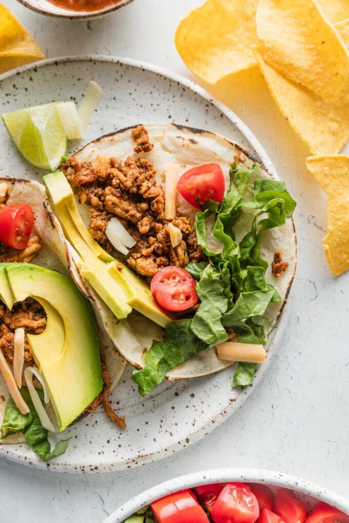 Close up of a ground chicken taco plated with avocado, tomato, cheese, and lettuce.