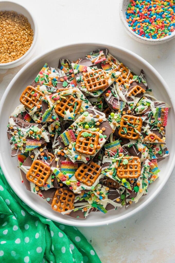 Large white plate piled high with leprechaun bark, a cute St. Patrick's-themed treat with chocolate, pretzels, candy, and sprinkles.
