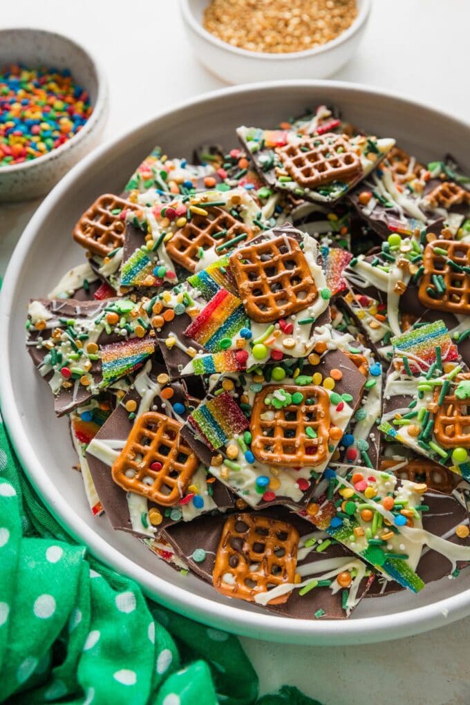 Angled view of a plate full of leprechaun bark, with extra rainbow and gold sprinkles in the back.