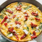 Angled view of an uncut frittata with feta, spinach, and sun-dried tomatoes.