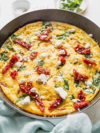 Angled view of an uncut frittata with feta, spinach, and sun-dried tomatoes.
