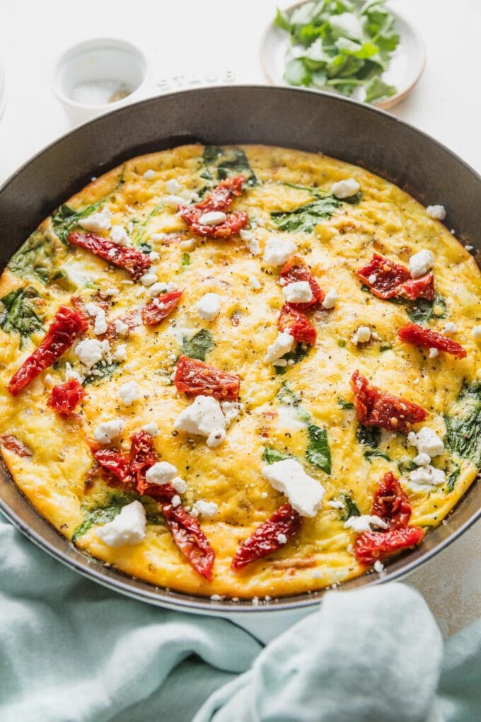 Angled view of an uncut frittata with feta, spinach, and sun-dried tomatoes.