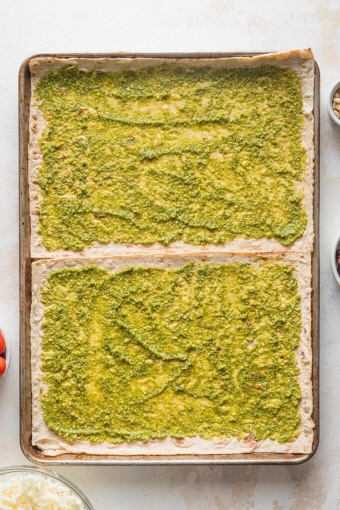 Thin layer of pesto spread on top of two flatbreads.