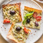 Small plate with three slices of pesto flatbread pizza garnished with extra fresh basil leaves and red pepper flakes.