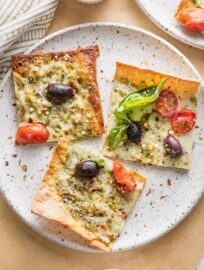 Small plate with three slices of pesto flatbread pizza garnished with extra fresh basil leaves and red pepper flakes.