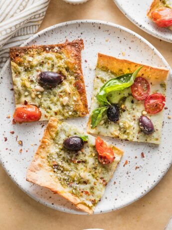 Small plate with three slices of pesto flatbread pizza garnished with extra fresh basil leaves and red pepper flakes.