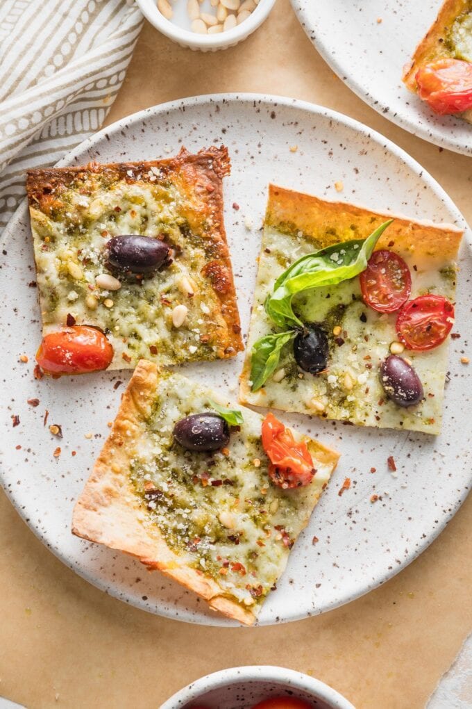 Small plate with three slices of pesto flatbread pizza garnished with extra fresh basil leaves and red pepper flakes.