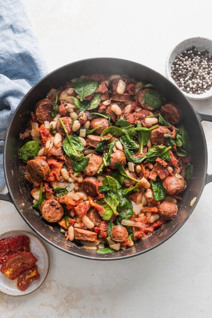 Deep cast-iron skillet filled with a simple dish of chicken sausage, white beans, spinach, and tomatoes.