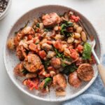 Shallow bowl with a generous helping of Tuscan style chicken sausage with white beans, spinach, and sun-dried tomatoes.