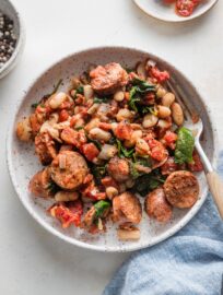 Shallow bowl with a generous helping of Tuscan style chicken sausage with white beans, spinach, and sun-dried tomatoes.