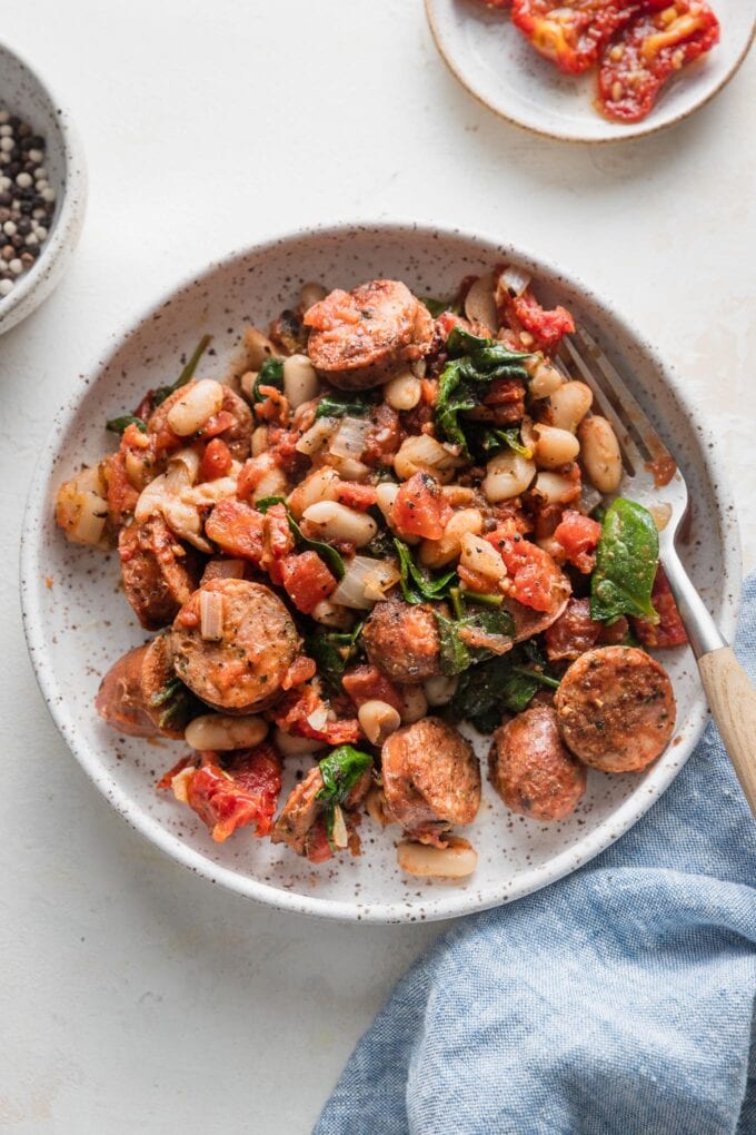 Shallow bowl with a generous helping of Tuscan style chicken sausage with white beans, spinach, and sun-dried tomatoes.