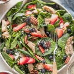 Large plate filled with a chicken spinach salad with berries, pecans, and feta.