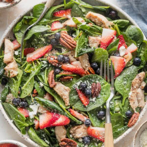 Large plate filled with a chicken spinach salad with berries, pecans, and feta.