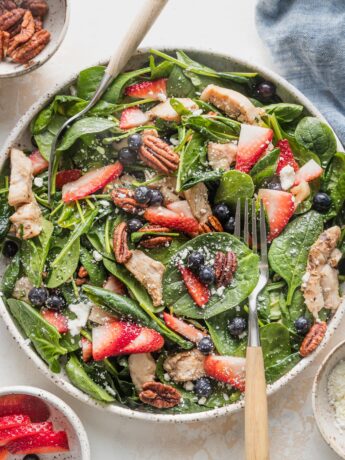 Large plate filled with a chicken spinach salad with berries, pecans, and feta.