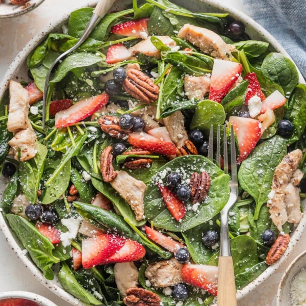 Large plate filled with a chicken spinach salad with berries, pecans, and feta.