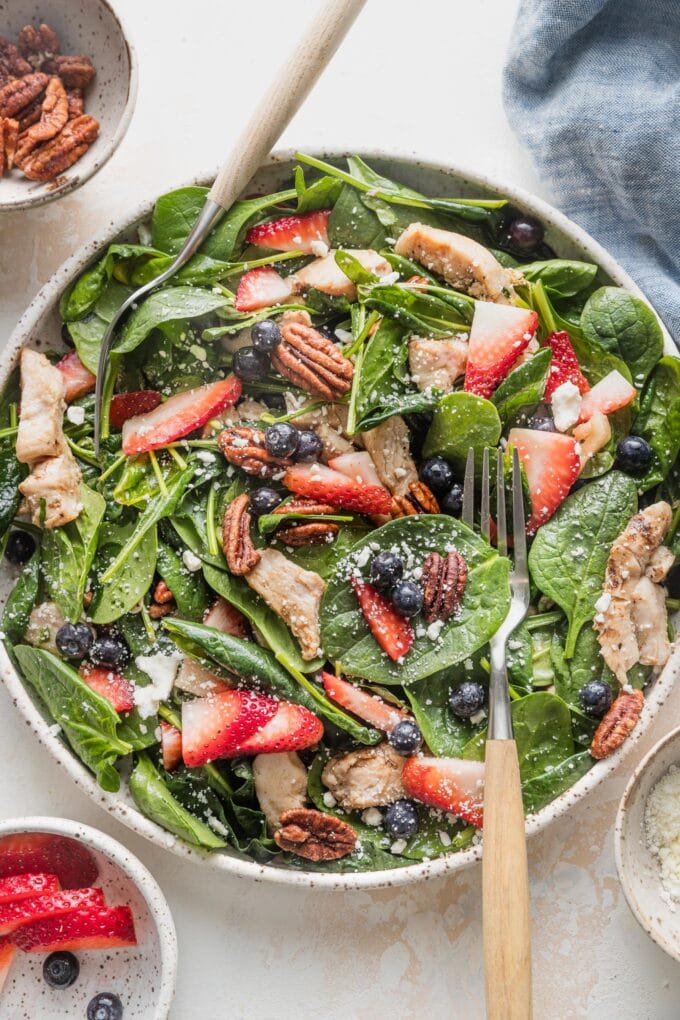 Large plate filled with a chicken spinach salad with berries, pecans, and feta.