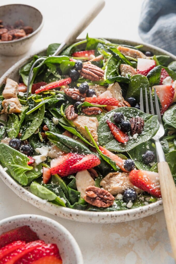 Angled view of a plated chicken spinach salad with strawberries, blueberries, and pecans.