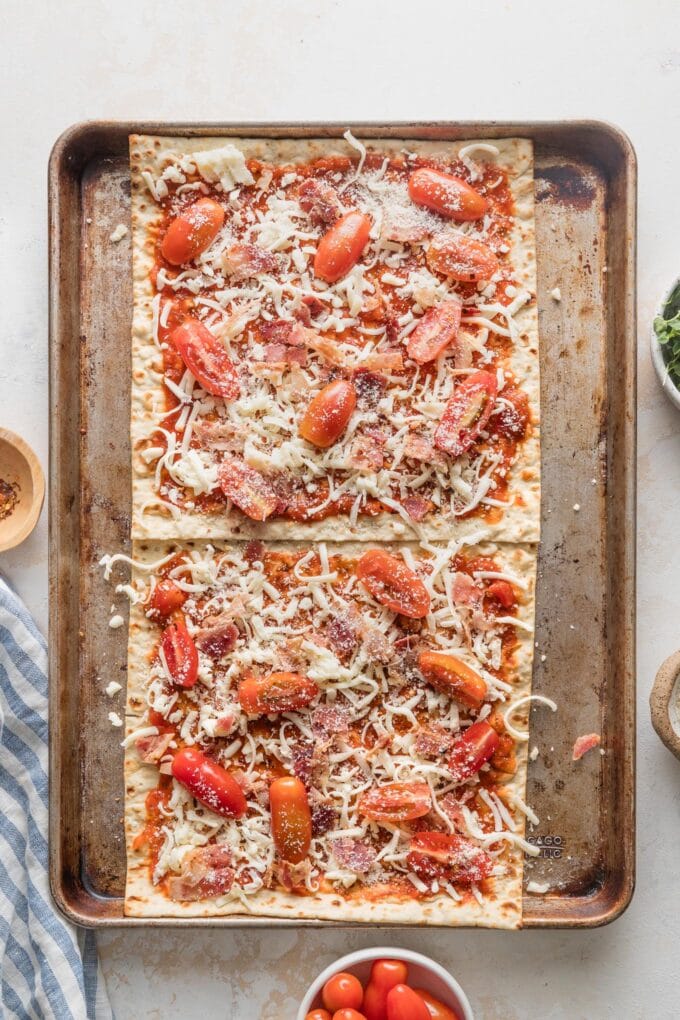 Sheet pan with partially-assembled BLT flatbreads, ready to bake.