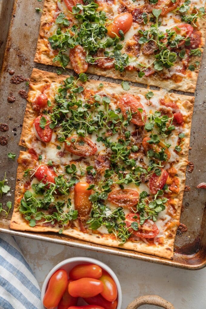 Two fully cooked BLT flatbreads on a sheet pan, just out of the oven and ready to slice and serve.