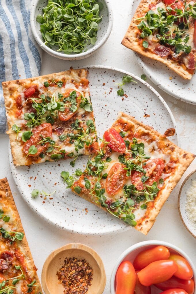 Ceramic speckled white plate with two slices of BLT flatbread pizza resting on a countertop.