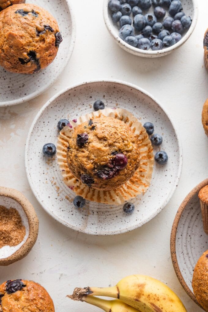 Overhead view of a banana blueberry muffin unwrapped from its liner and set on a small plate to eat.