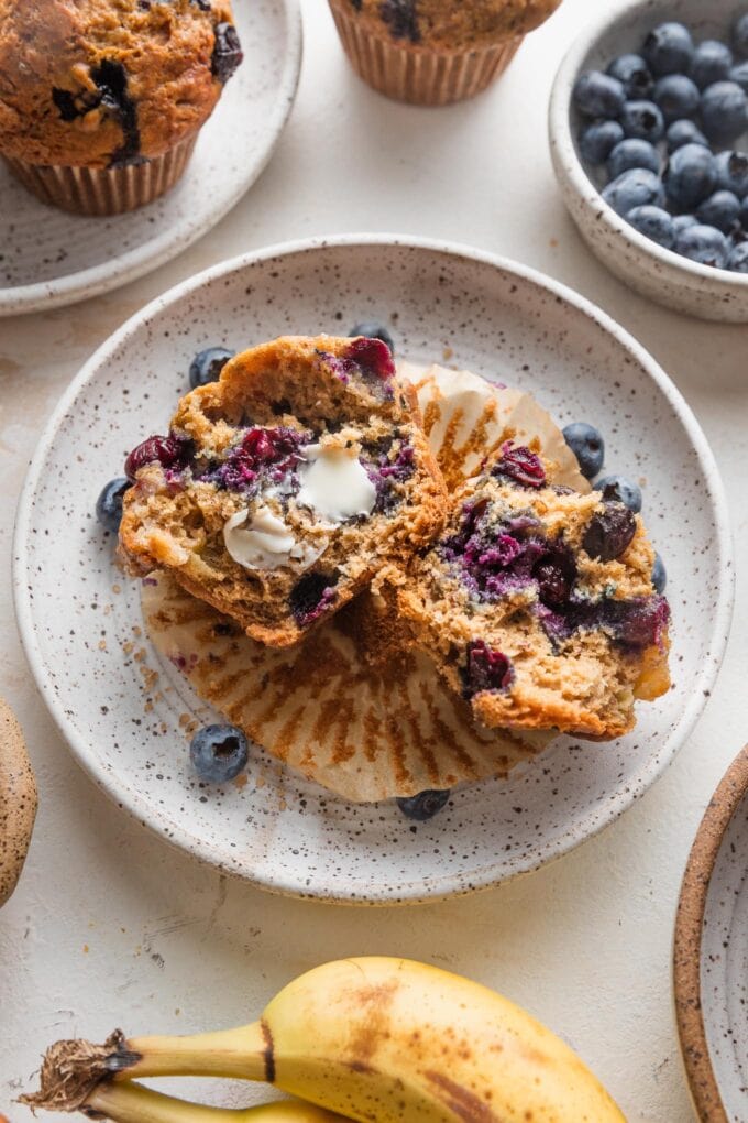 Blueberry banana muffin on a plate with butter smeared on the inside.