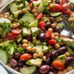 Angled view of a large bowl full of chickpea avocado salad with cucumber, tomato, and olives.
