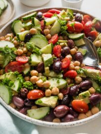 Angled view of a large bowl full of chickpea avocado salad with cucumber, tomato, and olives.