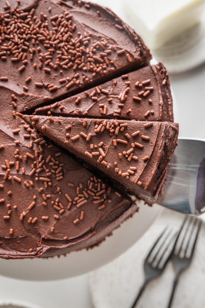 Overhead view of a chocolate layer cake starting to be sliced, with a cake server about to lift out the first piece.