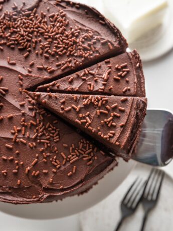 Overhead view of a sliced chocolate buttermilk layer cake with one slice being lifted up and away to serve.